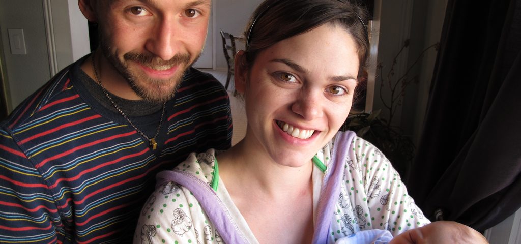 Two parents, presumanbly a father and mother with the mother holding a newborn baby.